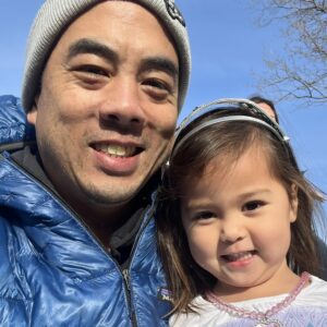 A father and daughter smiling together, the father wearing a blue puffer jacket