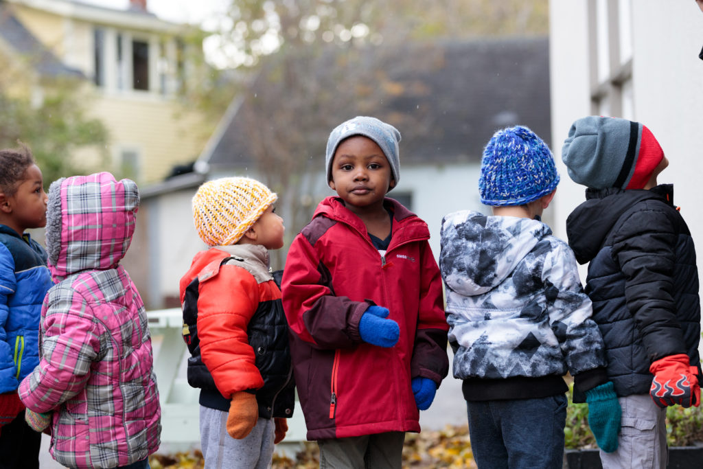 A row of young children wearing winter hats and coats waiting in a line