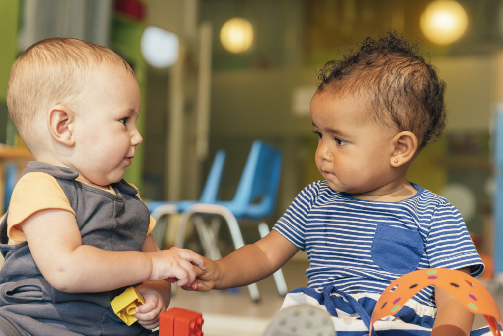 Two babies play together sitting on the floor with toys