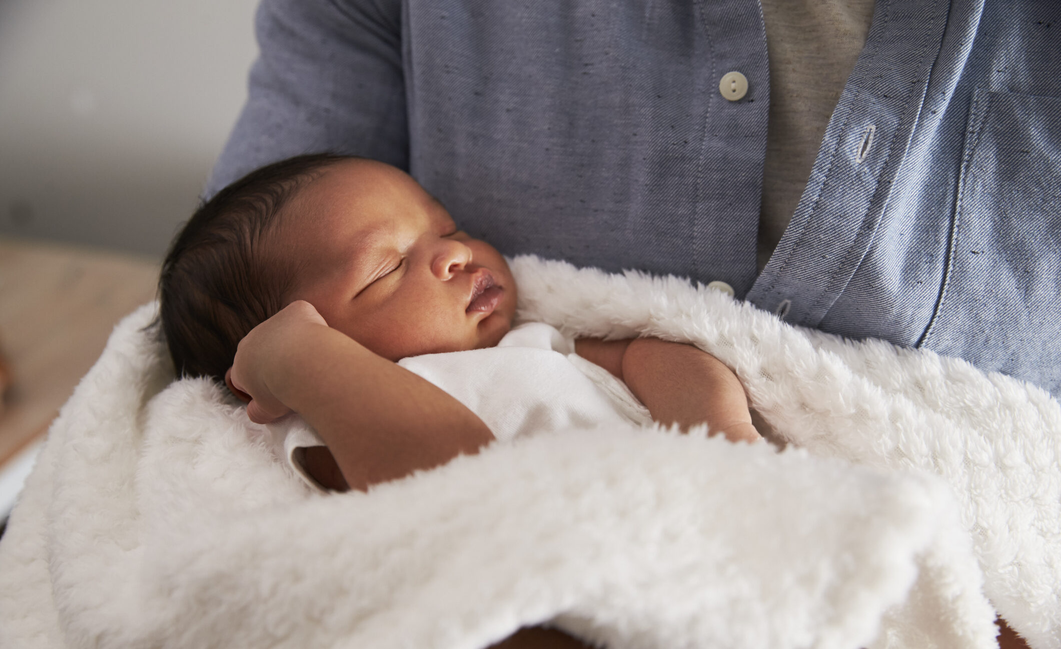 A very young baby with brown skin and black hair is held lovingly in their parent's arms