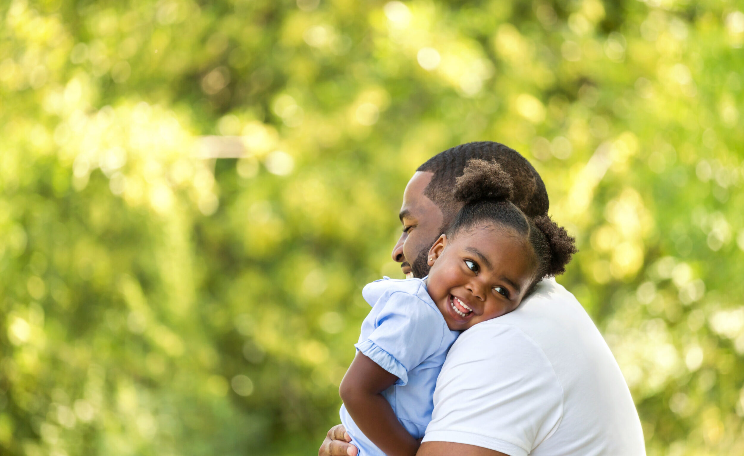 African American father hugging his young daughter, who smiles happily