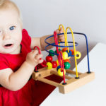 A baby with light skin and light hair plays with a colorful baby toy with beads on tracks