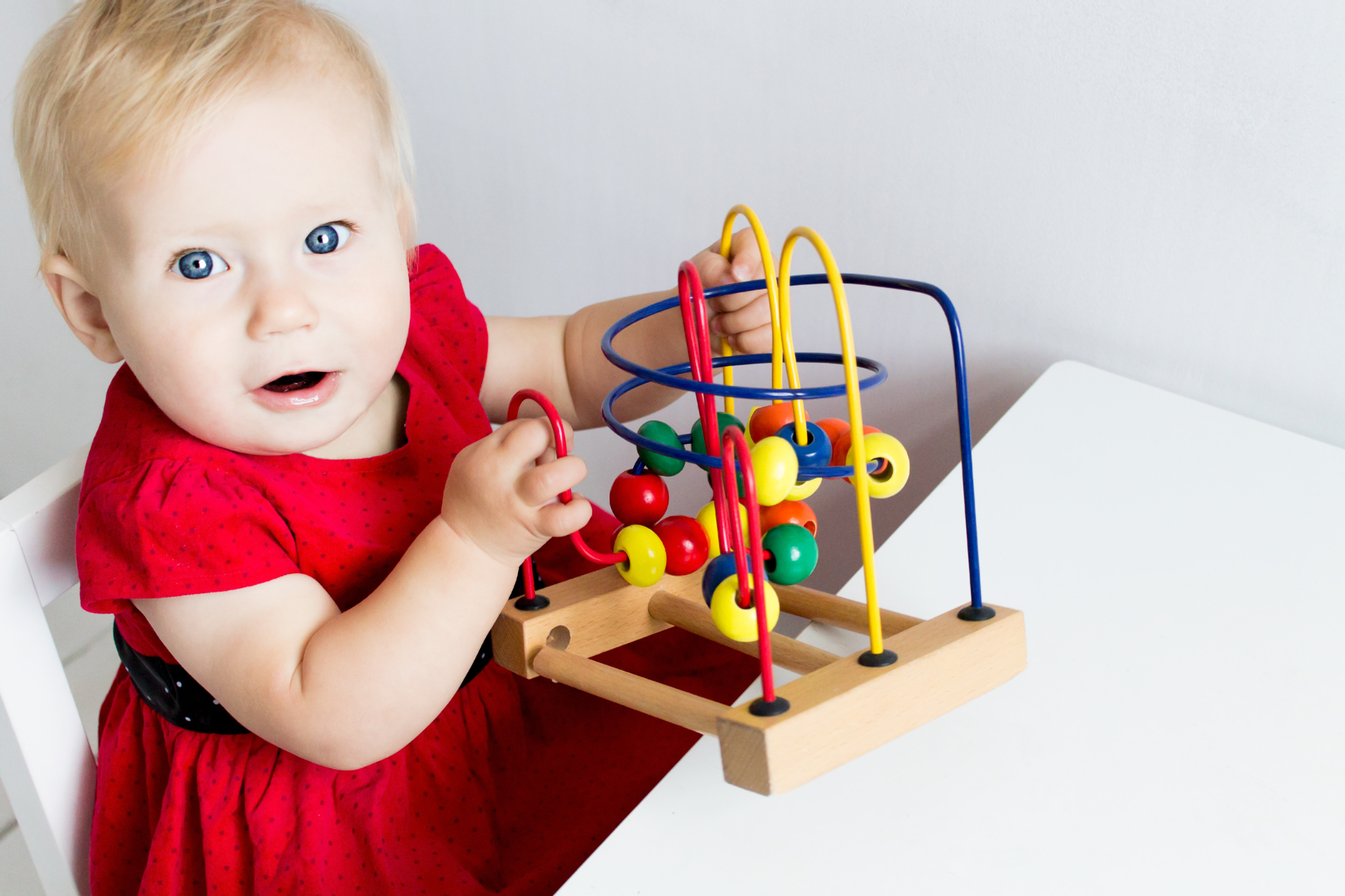 A baby with light skin and light hair plays with a colorful baby toy with beads on tracks