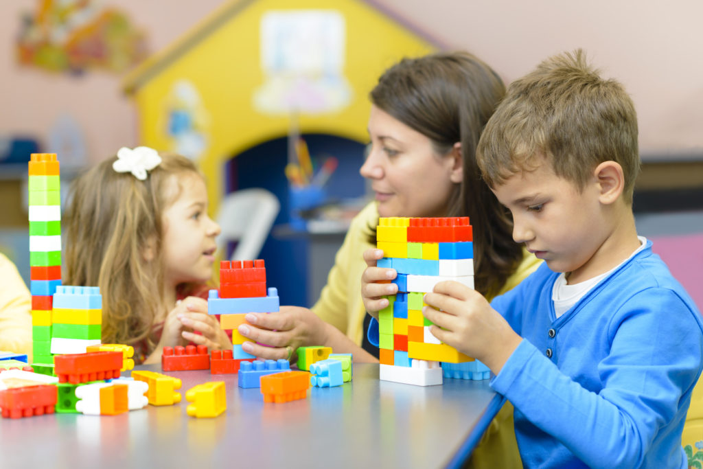 A white woman sits with two young children playing with plastic building blocks