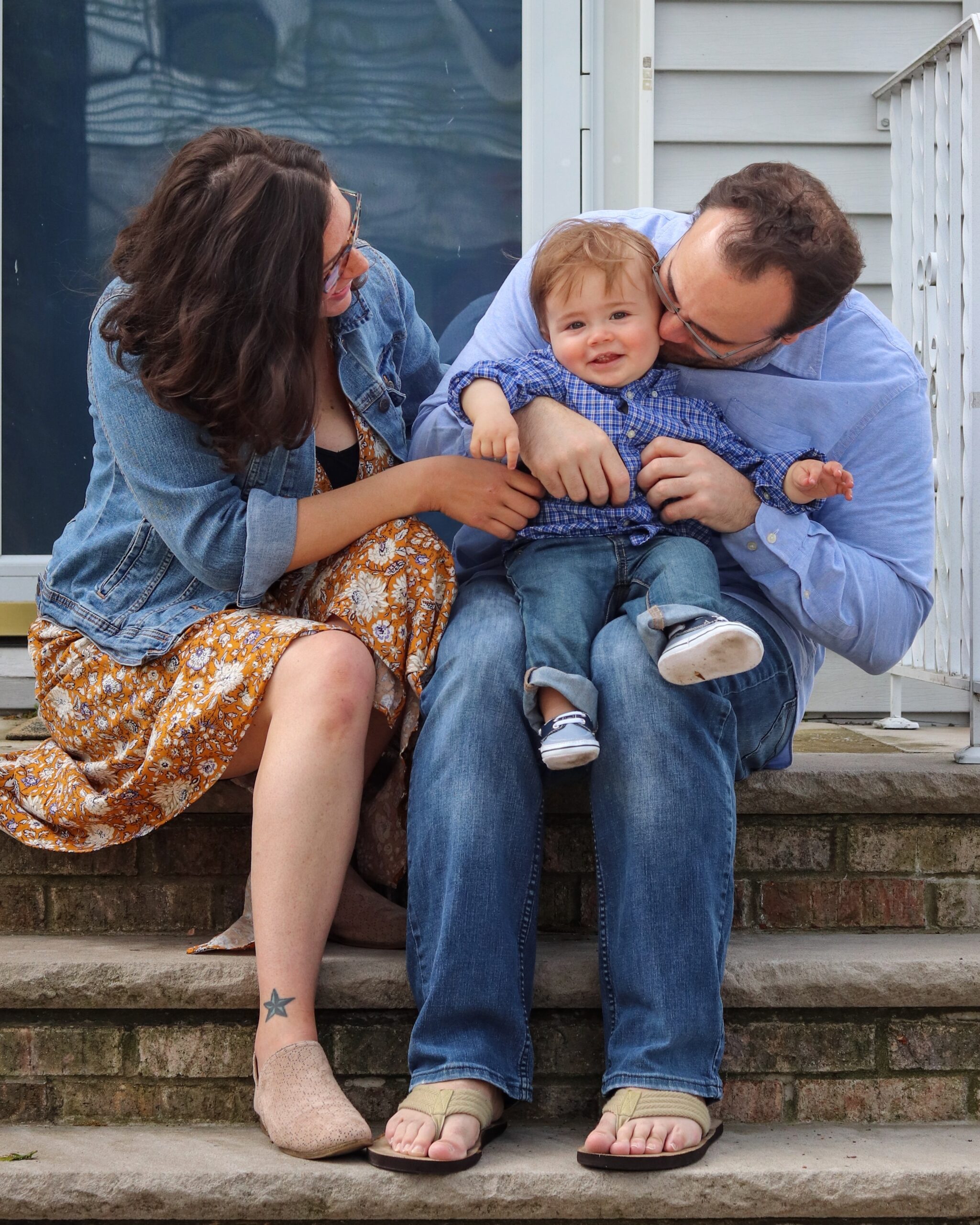 Two white parents embrace their young child while sitting on a stoop