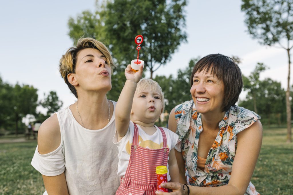 Two white women with a young child blowing bubbles and smiling