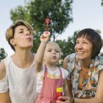 Two white women with a young child blowing bubbles and smiling