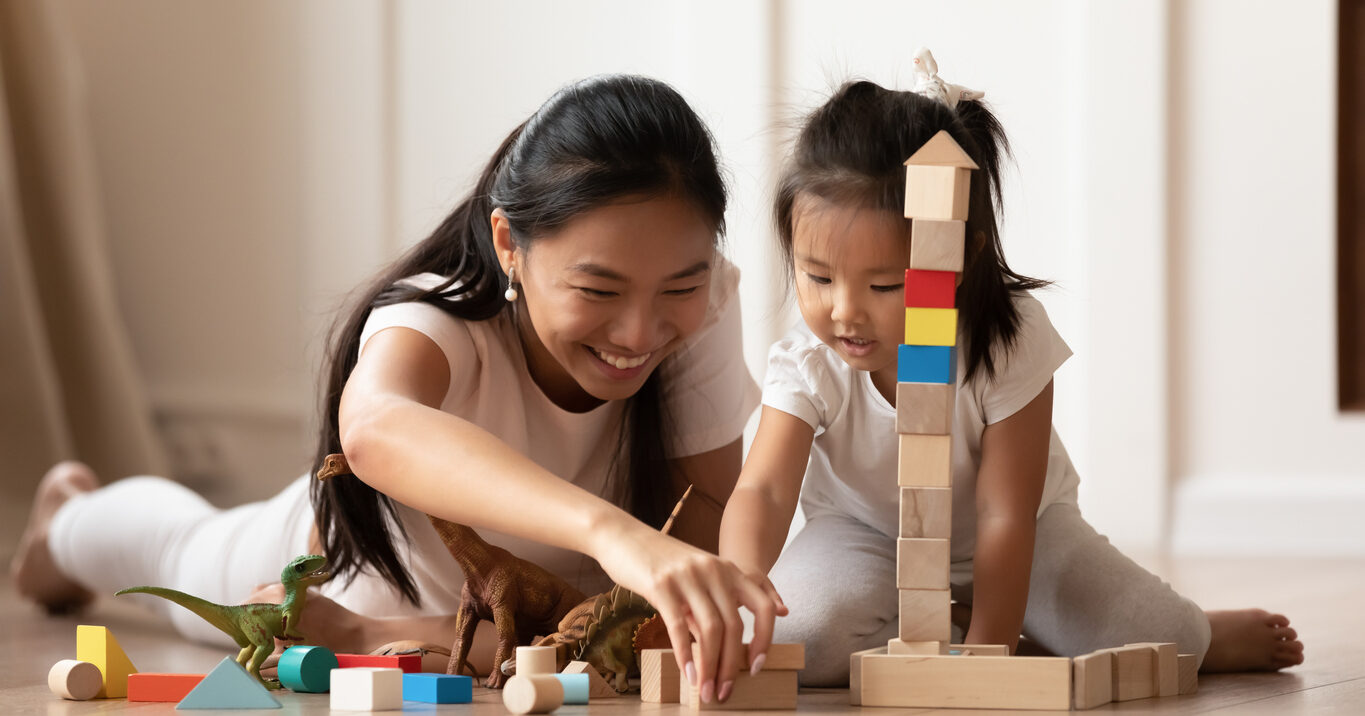 Smiling Vietnamese mom and young daughter play with blocks at home