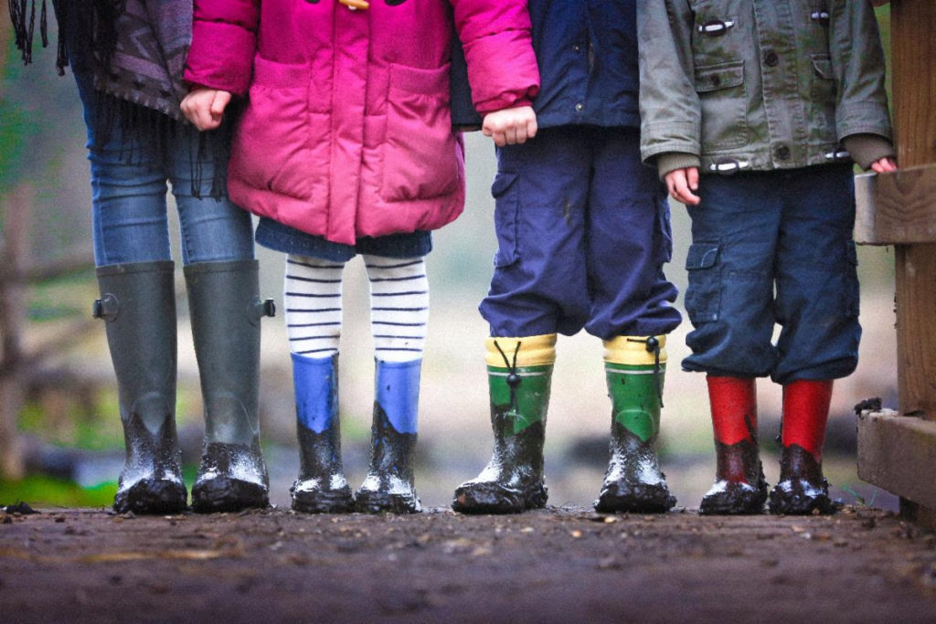 Four children, shown from the waist down, wearing coats and mud-covered rain boots