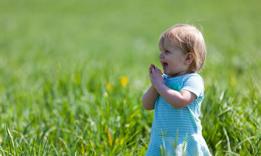 Young toddler smiling in a field of green grass