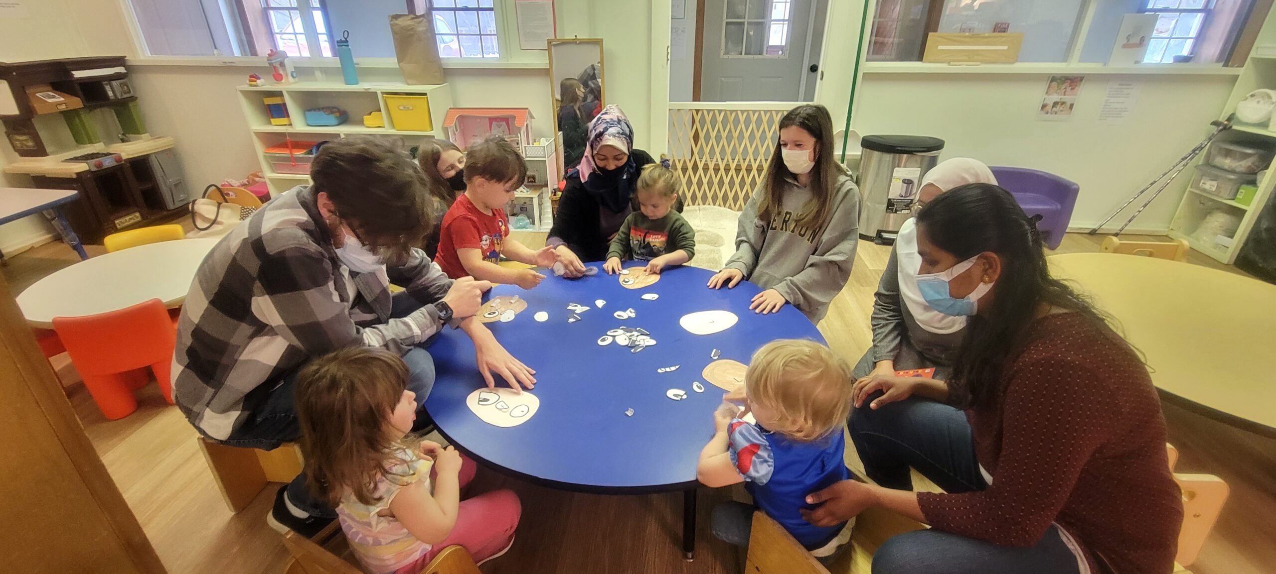 Young children and teachers around a table in a classroom