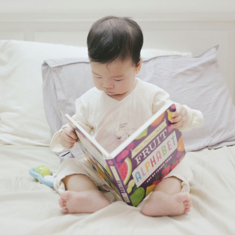 An Asian baby holds a picture book called Fruit Alphabet