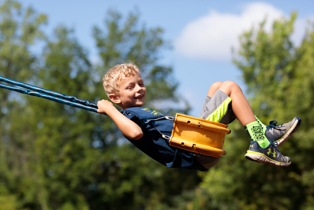 A young boy with blond hair and light skin swings happily on a swing