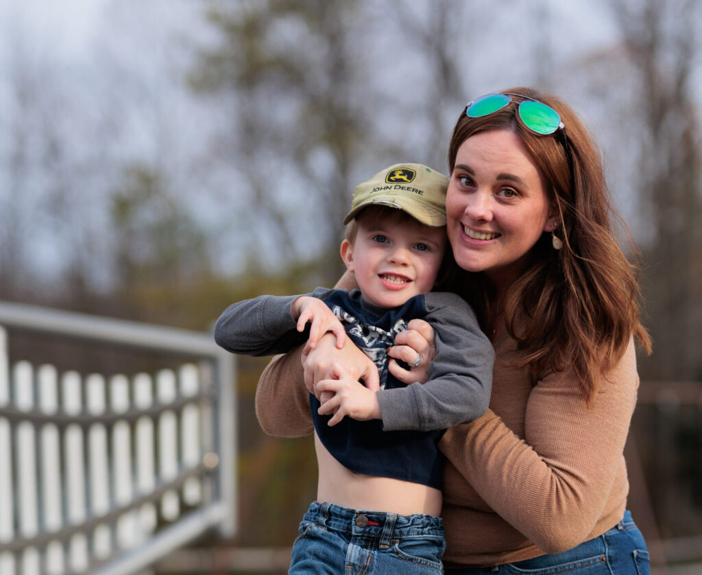 A smiling mom holds up her young son at a playground