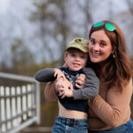 A smiling mom holds up her young son at a playground