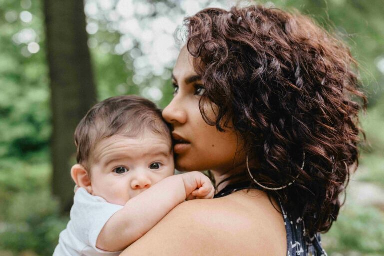 A young mom with dark curly hair holds her baby in her arms