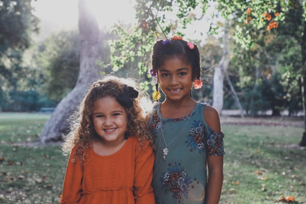 Two young girls with brown skin stand together smiling in a grassy yard