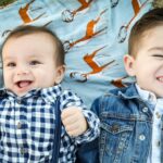 Two young brothers with brown hair smile while lying on a picnic blanket