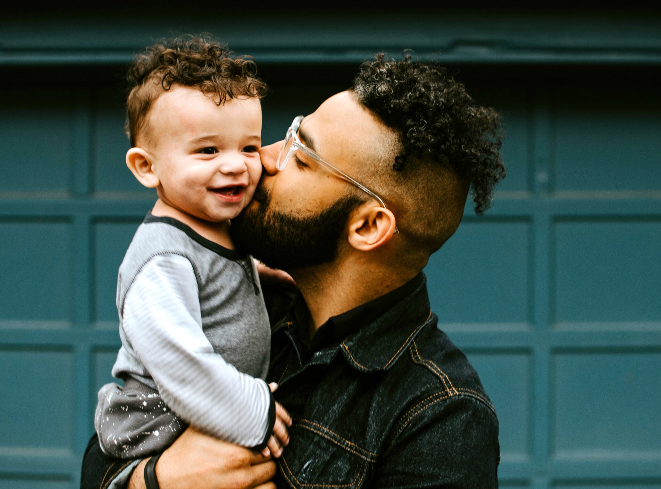 A Black dad with glasses holds his happy toddler in his arms