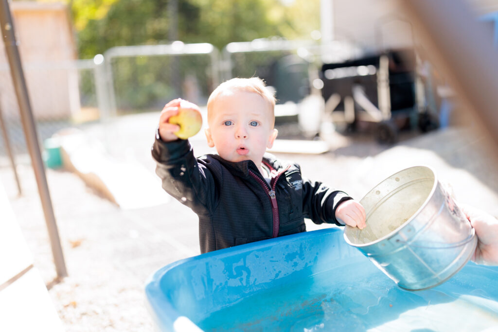 A toddler with blond hair holds up an apple