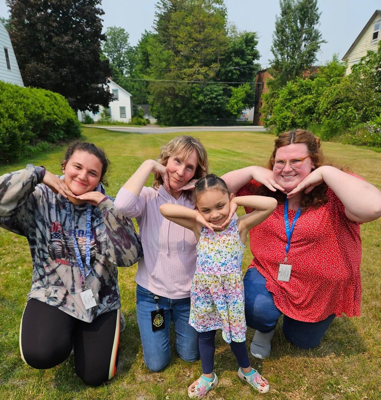 Three women and a young child pose together, smiling with their hands held under their chins