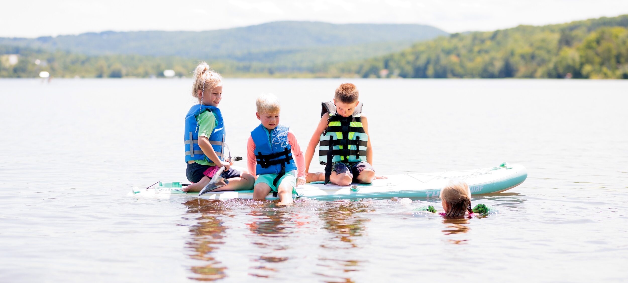 Four young kids wearing life jackets play on a paddleboat on Lake Elmore