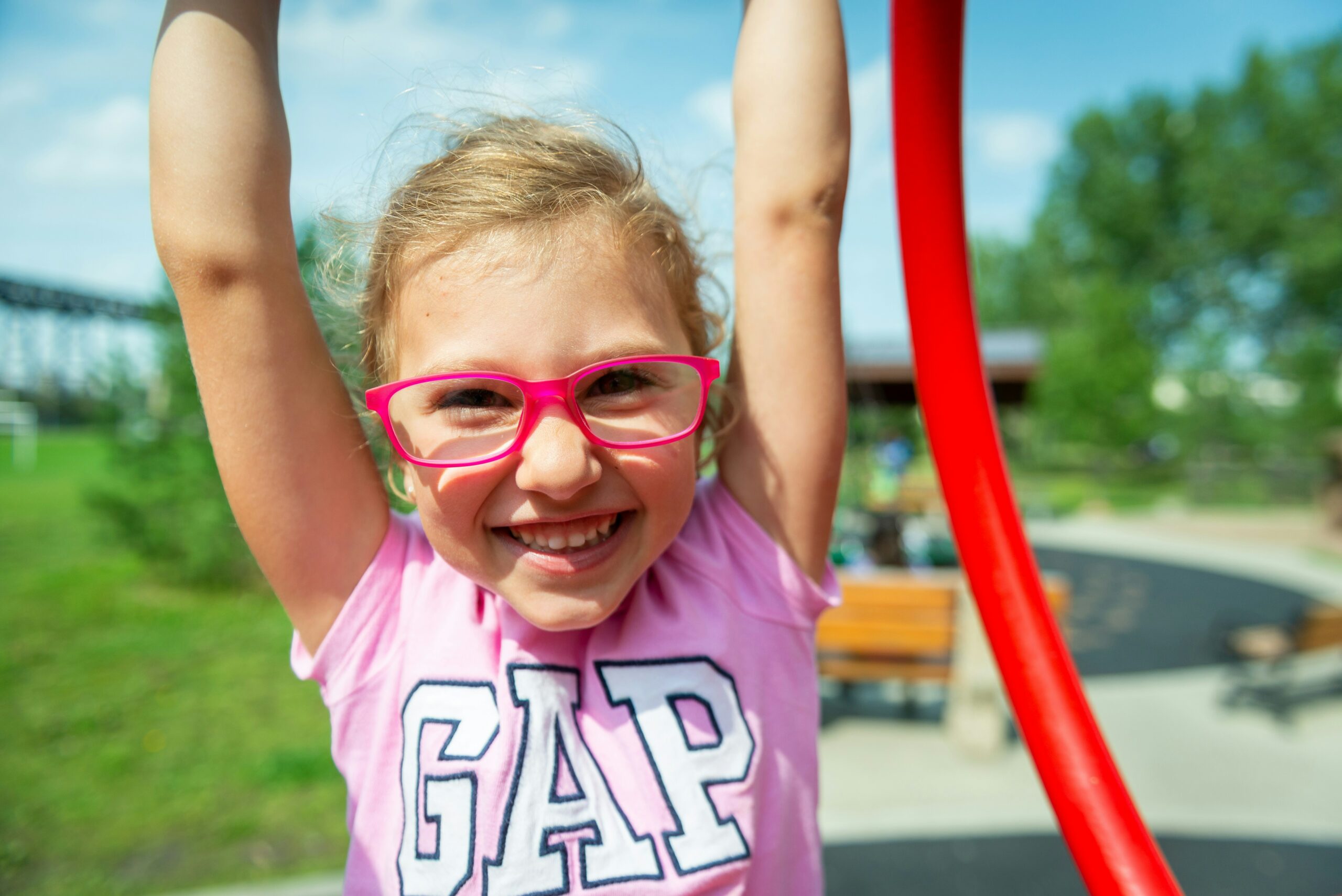 A young child wearing glasses and smiling as she raises her arms up overhead