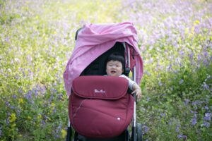 Smiling infant in stroller with stroller cover, with pink sweatshirt draped on stroller handle