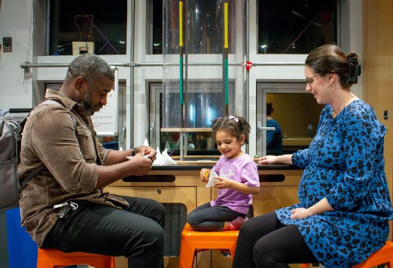 Two adults and a young child doing a project with paper at ECHO, Leahy Center for Lake Champlain