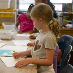 Young child with ponytail sitting at table in classroom drawing