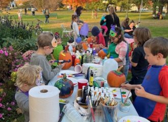 Children paint pumpkins outdoors at Fall Fun Fridays in Lyndonville