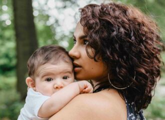 A young mom with dark curly hair holds her baby in her arms