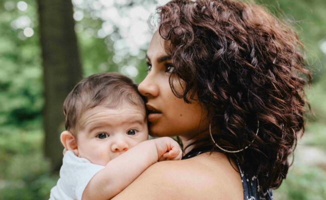 A young mom with dark curly hair holds her baby in her arms