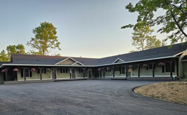 Exterior of the Stay & Play Child Care Center in Lyndonville, VT, showing sage-green siding and hanging flower baskets