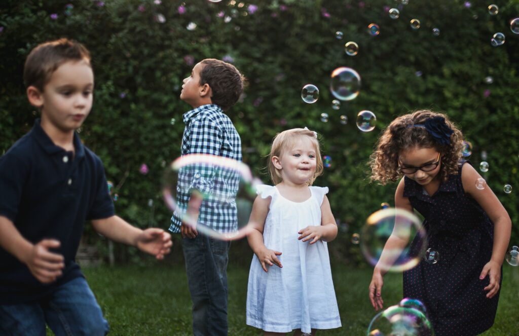 Four young children of various ages play outside with bubbles