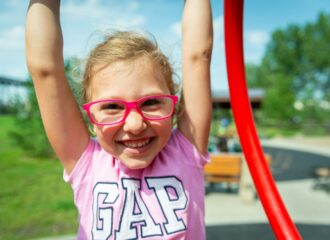 A young child wearing glasses and smiling as she raises her arms up overhead