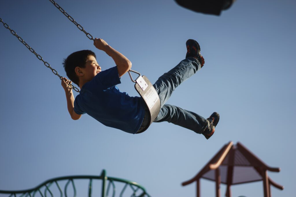 A young boy swings on a playground swing while smiling