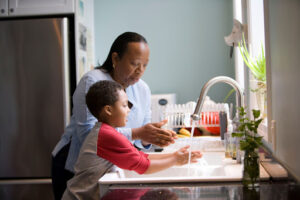 Parent and child washing hands at kitchen sink