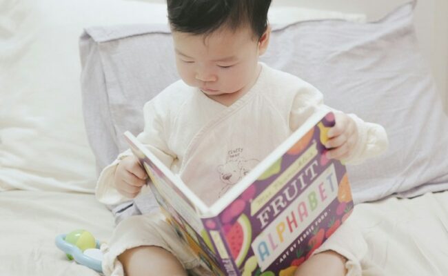 An Asian baby holds a picture book called Fruit Alphabet