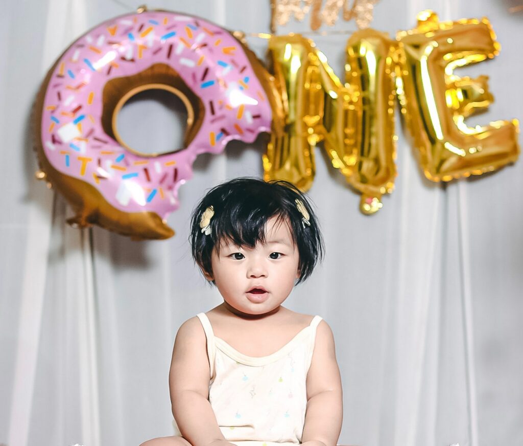 Young girl celebrating her first birthday with balloons spelling out "ONE"